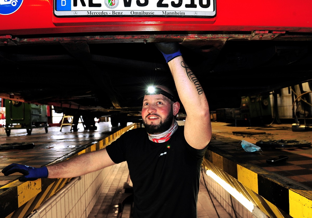 Vestische Werkstattmitarbeiter mit Kopflampe unter einem Bus.